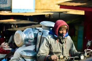 a man on a motorcycle carrying several milk cans  and a sack